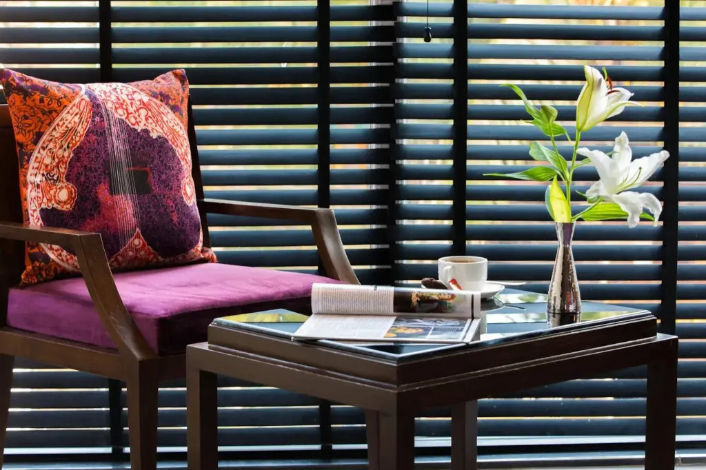 Une chaise violette avec un coussin repose devant des stores en bois.