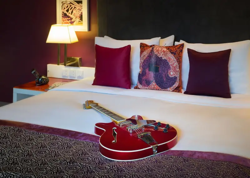 Un lit blanc est orné de coussins bordeaux et d'une guitare rouge.
