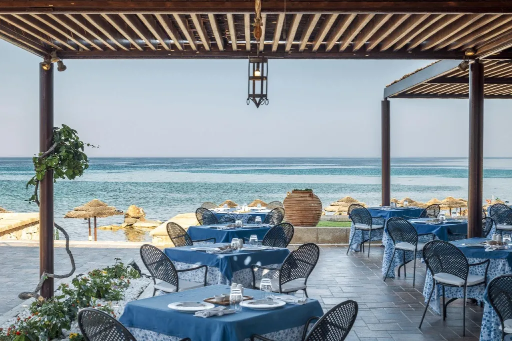 Tables dressées à l'ombre d'une pergola face à la mer.