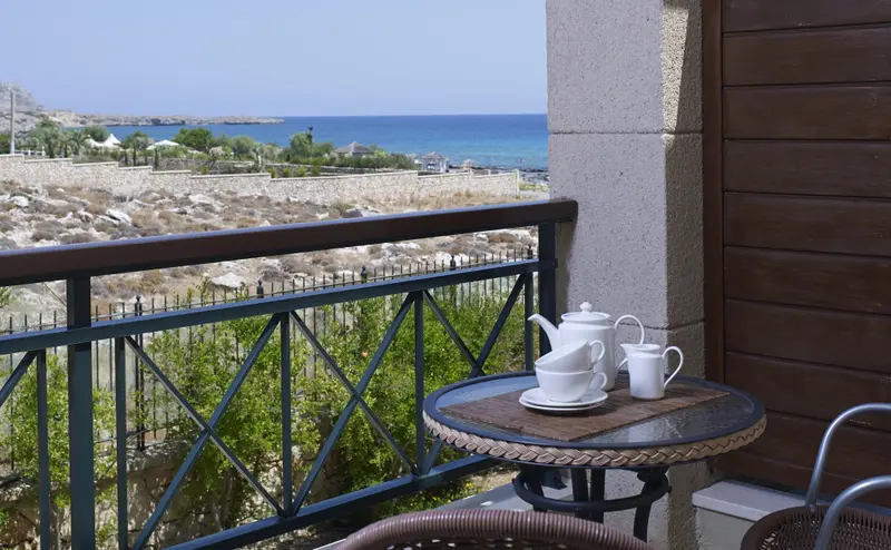 Une table ronde en mosaïque avec une théière et des tasses sur un balcon avec vue sur la mer.