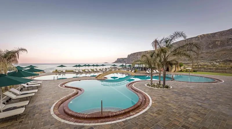 Piscine extérieure avec chaises longues et végétation luxuriante, face à la mer.