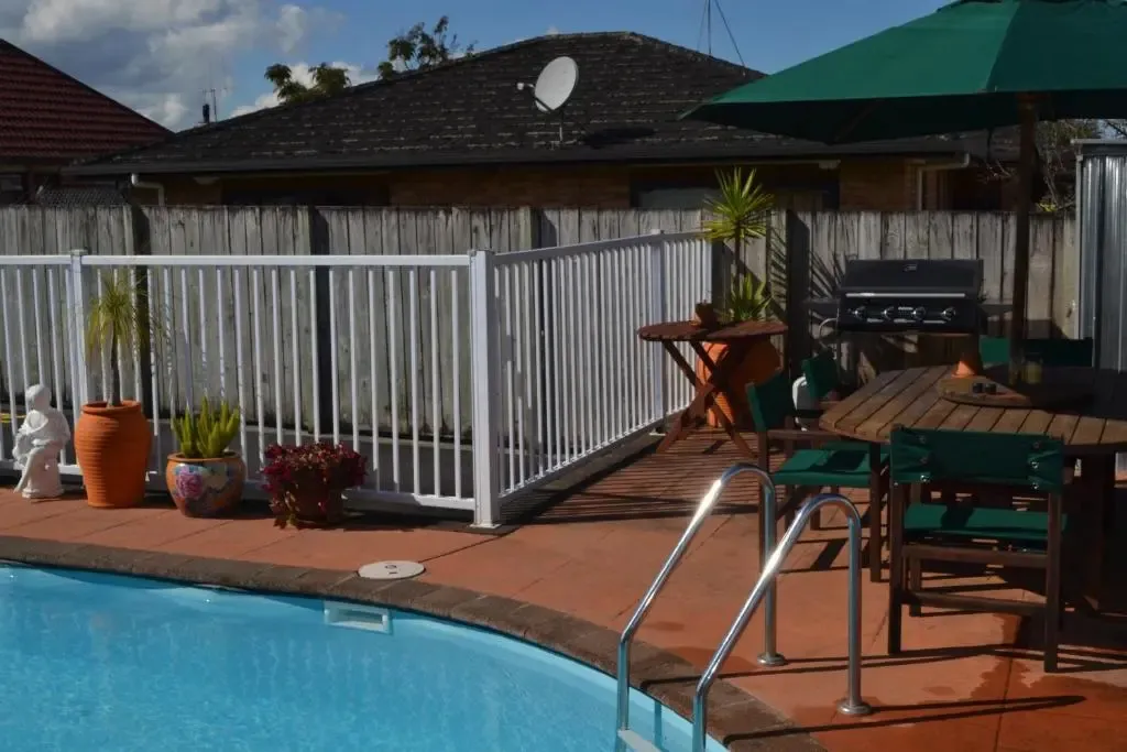 Une piscine avec une terrasse ensoleillée et un barbecue.