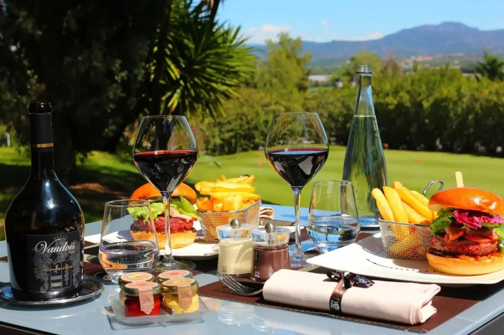 Une table est dressée avec des plats et des boissons, offrant une vue sur un terrain de golf verdoyant et des collines en arrière-plan.
