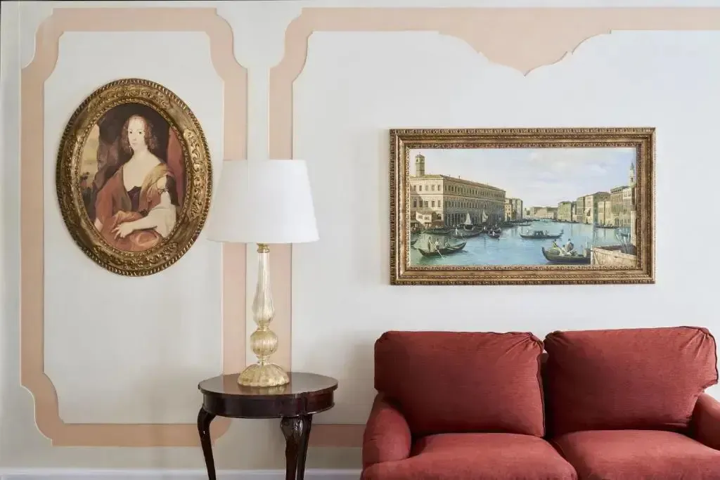 Un canapé rouge est placé devant un mur décoré de tableaux et d'une lampe sur une petite table.