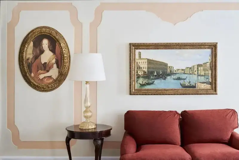Un canapé rouge est placé devant un mur décoré de tableaux et d'une lampe sur une petite table.