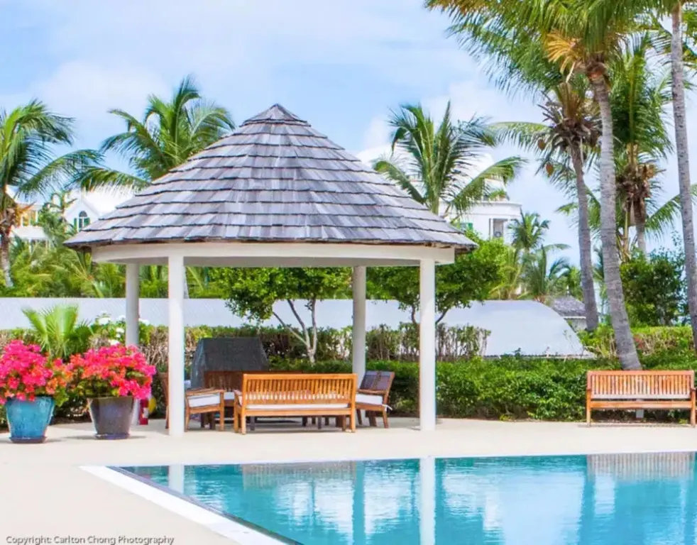Un pavillon ombragé offre un espace de détente près d'une piscine turquoise.