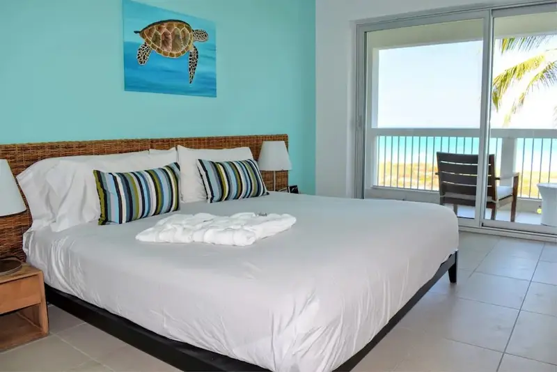 Une chambre lumineuse avec un grand lit face à une baie vitrée donnant sur la mer.