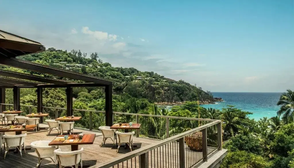 Terrasse avec tables et chaises donnant sur la mer et la végétation.