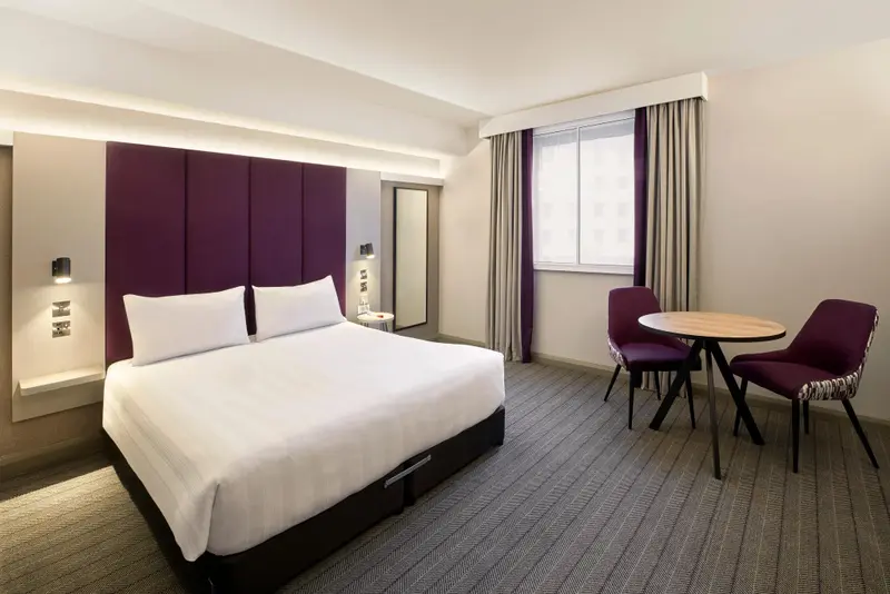 Une chambre lumineuse avec un lit double et un coin repas près d'une fenêtre.