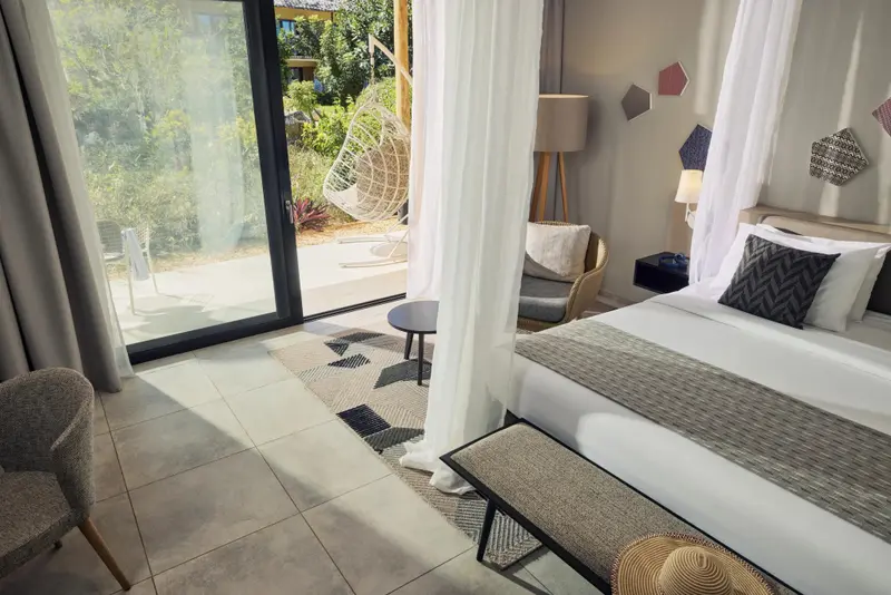 Une chambre lumineuse avec un lit recouvert d'une courtepointe blanche et un accès à une terrasse.