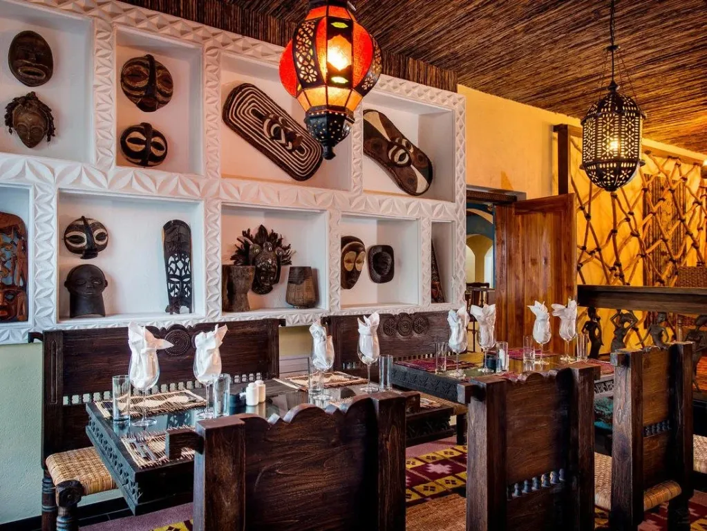 Une salle de restaurant décorée de masques africains et éclairée par des lanternes.