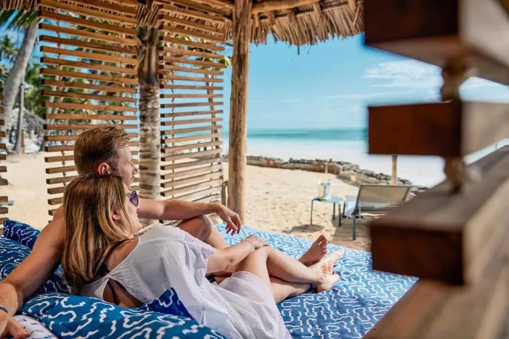 Un couple se détend sur des coussins face à une plage de sable blanc.