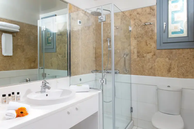 Une salle de bain lumineuse avec douche vitrée et vasque blanche.