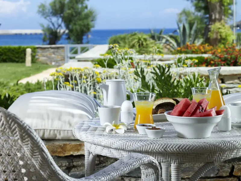 Une table de petit-déjeuner est dressée sur une terrasse ensoleillée avec vue sur la mer.