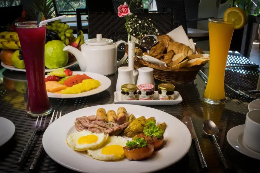 Une table est dressée avec un copieux petit-déjeuner composé de fruits, de viennoiseries et d'oeufs.