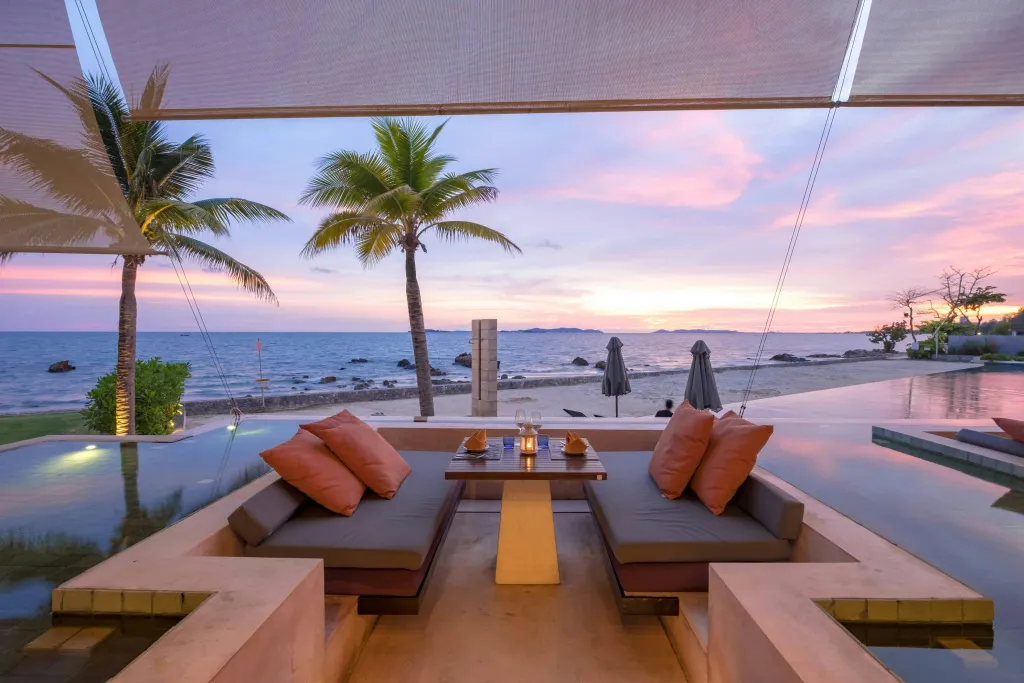 Espace de détente avec canapés et table basse au bord d'une piscine face à la mer au coucher du soleil.