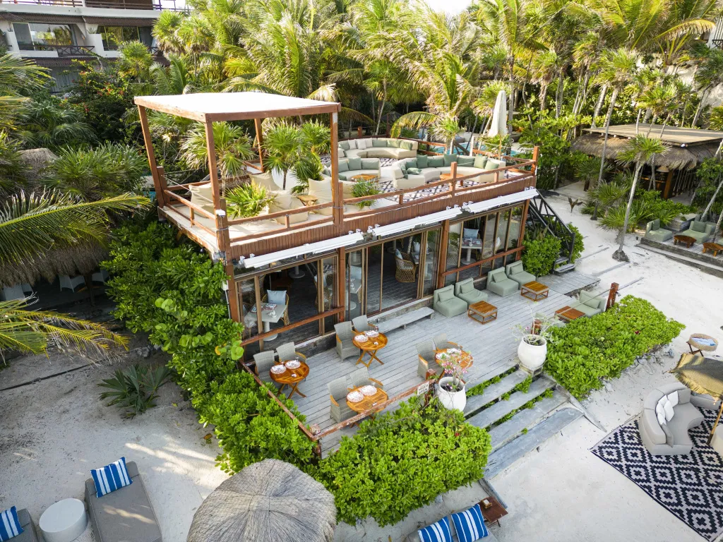 Bâtiment moderne avec terrasses et mobilier de jardin au bord d'une plage de sable blanc.