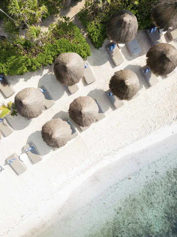 Vue aérienne d'une plage de sable blanc avec des parasols en chaume et des transats.