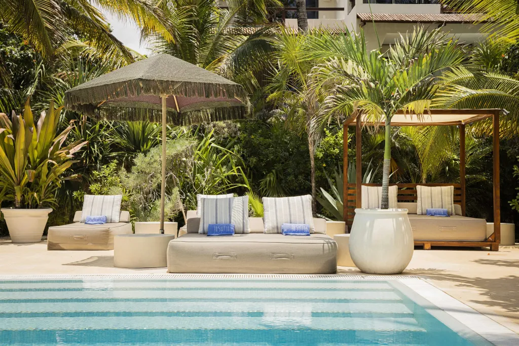 Mobilier de détente au bord d'une piscine ombragée par des parasols et des palmiers.