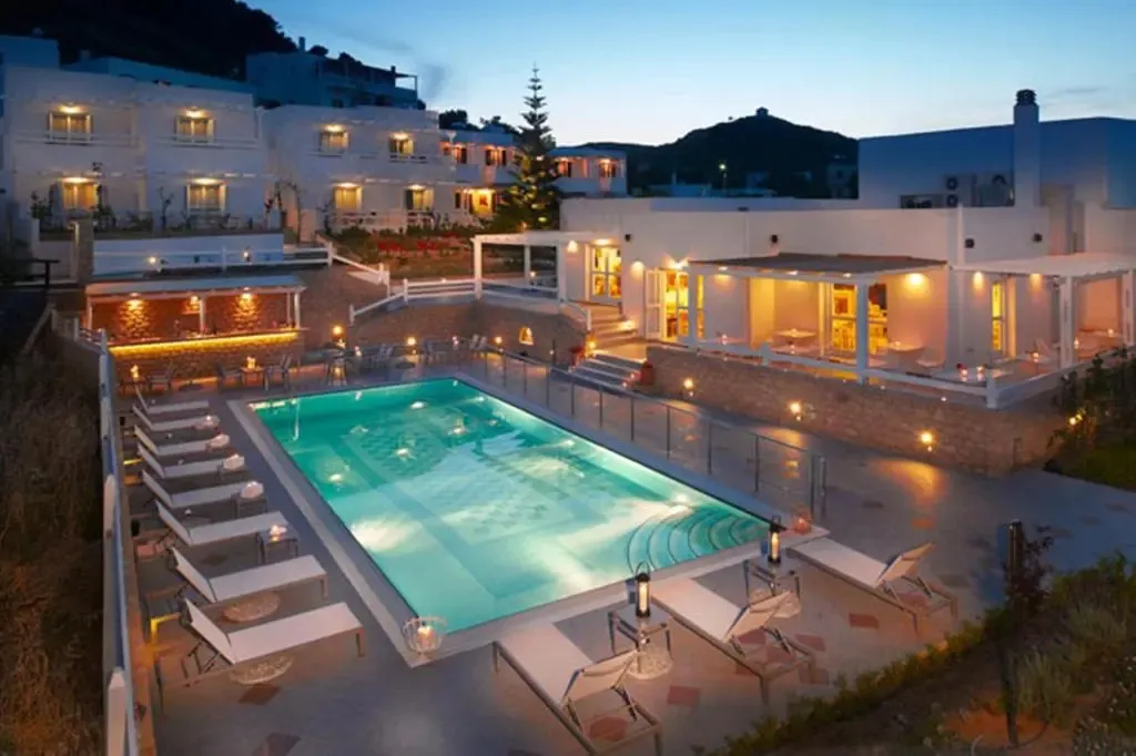 Piscine rectangulaire illuminée avec chaises longues et bâtiment blanc en arrière-plan.