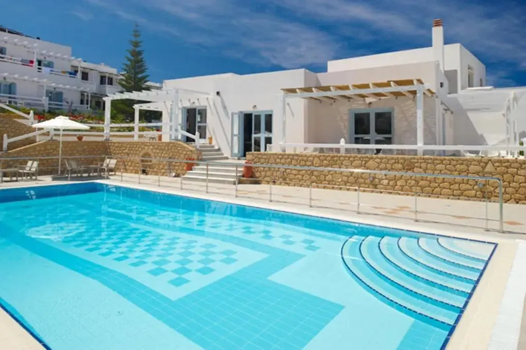 Piscine bleue devant un bâtiment blanc avec une pergola ombragée.