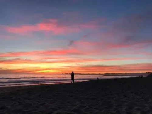 Une plage au coucher du soleil avec une personne debout sur le sable.