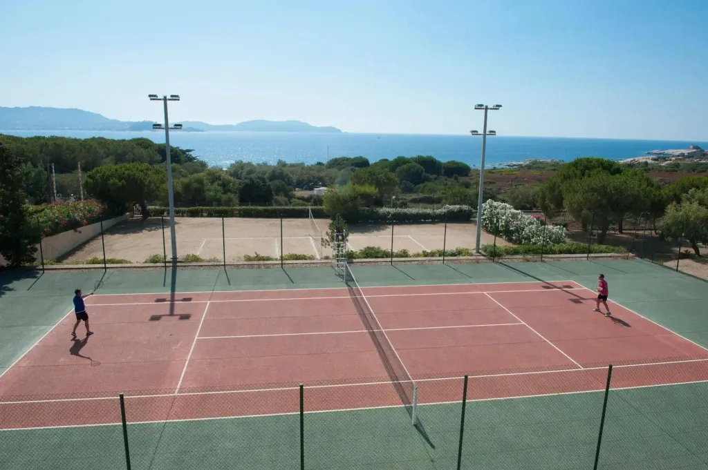 Deux personnes jouent au tennis sur un court en terre battue avec vue sur la mer.