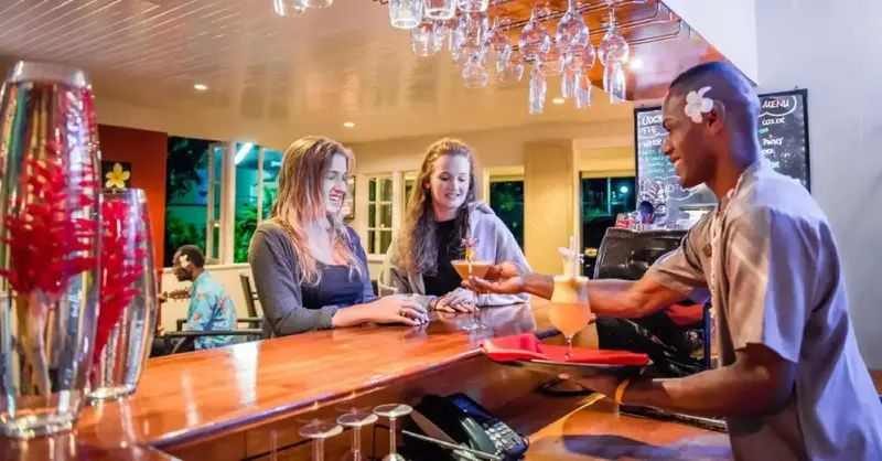 Un barman prépare des cocktails pour deux clientes assises au comptoir.