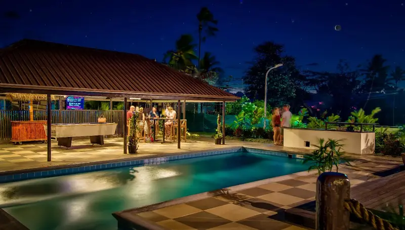 Une piscine illuminée avec un bar en arrière-plan et des personnes discutant.