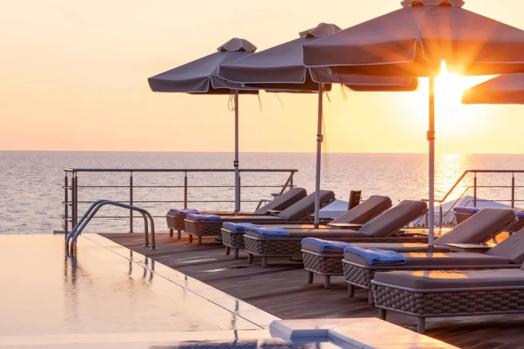 Transats et parasols bordent une piscine à débordement face à la mer au coucher du soleil.