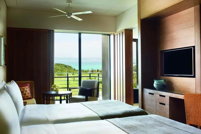 Une chambre lumineuse avec un lit double et une vue sur un terrain de golf et la mer.