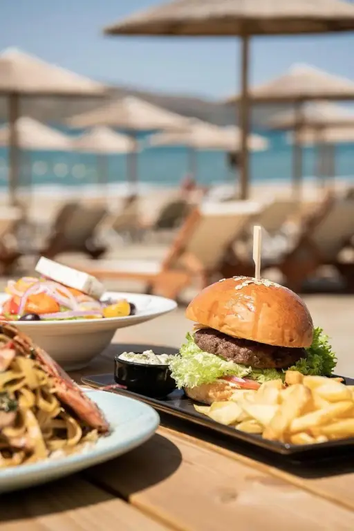 Une table en bois présente des plats variés avec en arrière-plan une plage et des parasols.