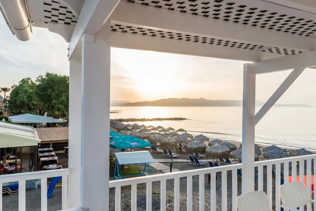 Vue sur la mer et la plage depuis une terrasse ombragée.