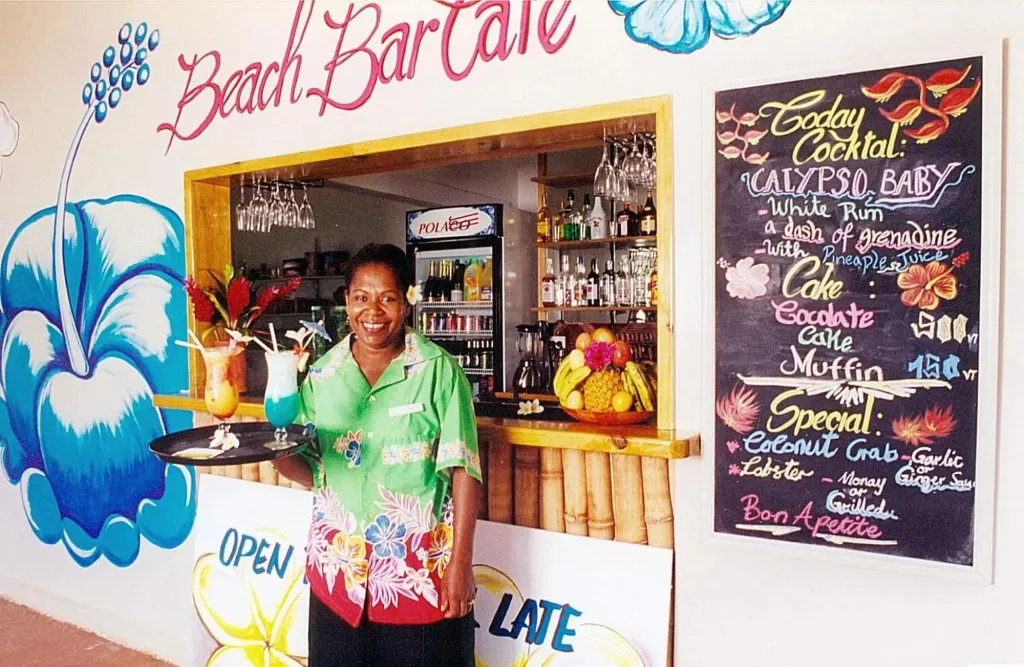 Une personne souriante présente des boissons colorées devant un comptoir de bar décoré.