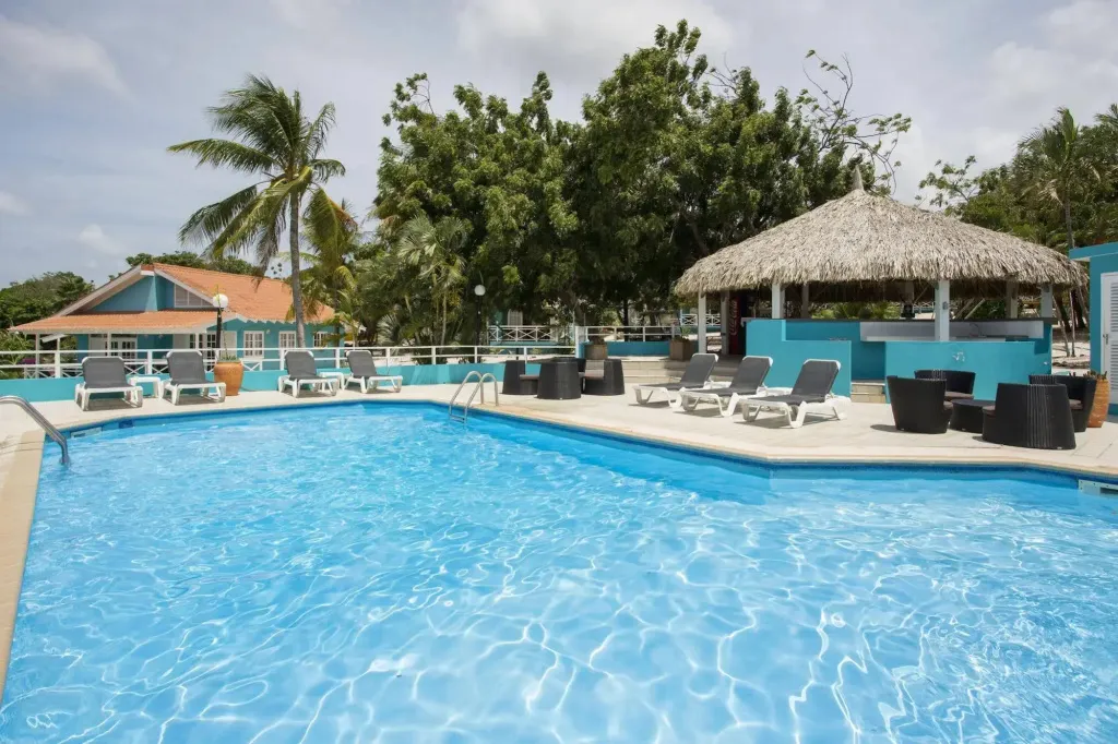 Une piscine turquoise bordée de transats et d'un espace ombragé.