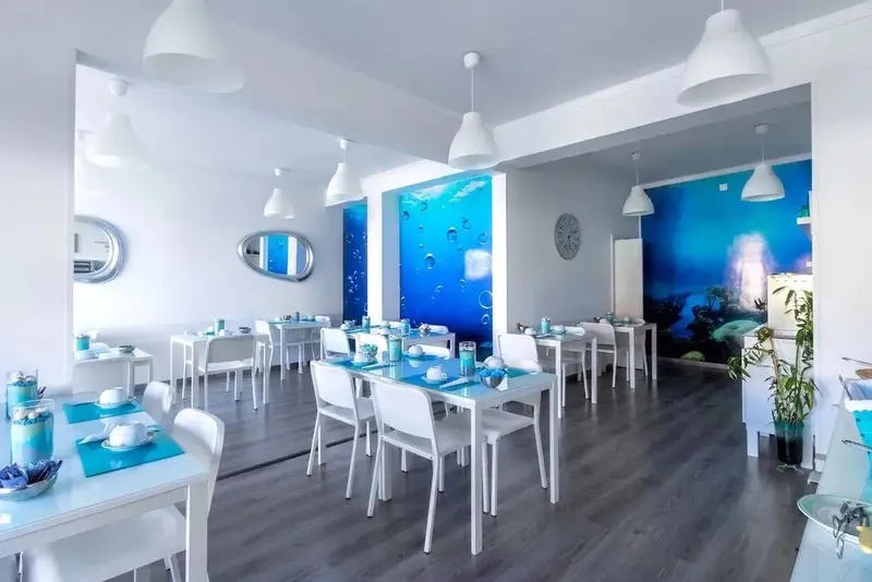 Une salle lumineuse est aménagée avec des tables et des chaises blanches, prêtes pour le service.