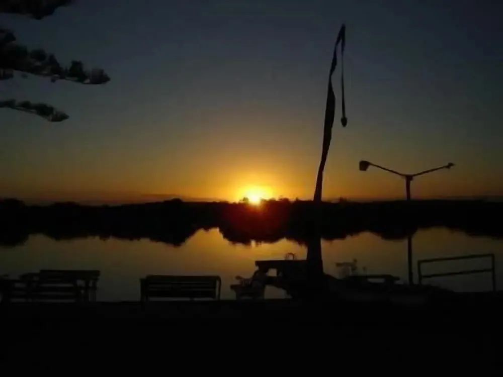 Coucher de soleil sur une étendue d'eau calme avec des silhouettes de mobilier urbain.