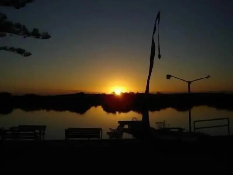 Coucher de soleil sur une étendue d'eau calme avec des silhouettes de mobilier urbain.