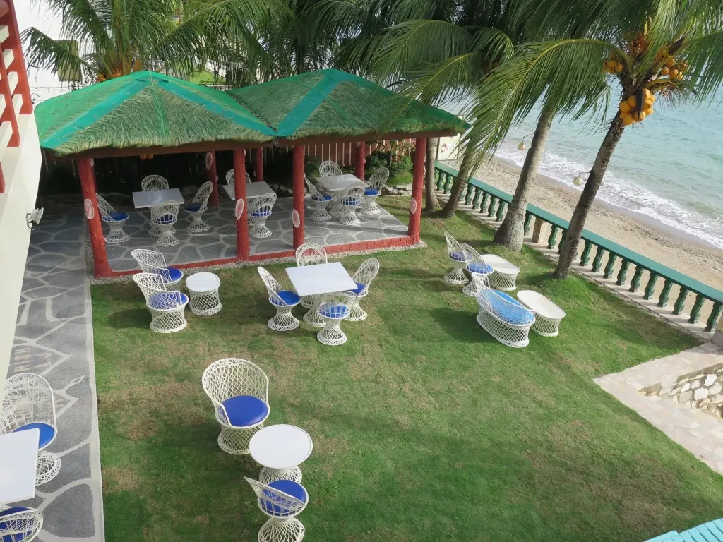 Terrasse ombragée avec tables et chaises donnant sur une plage de sable fin.