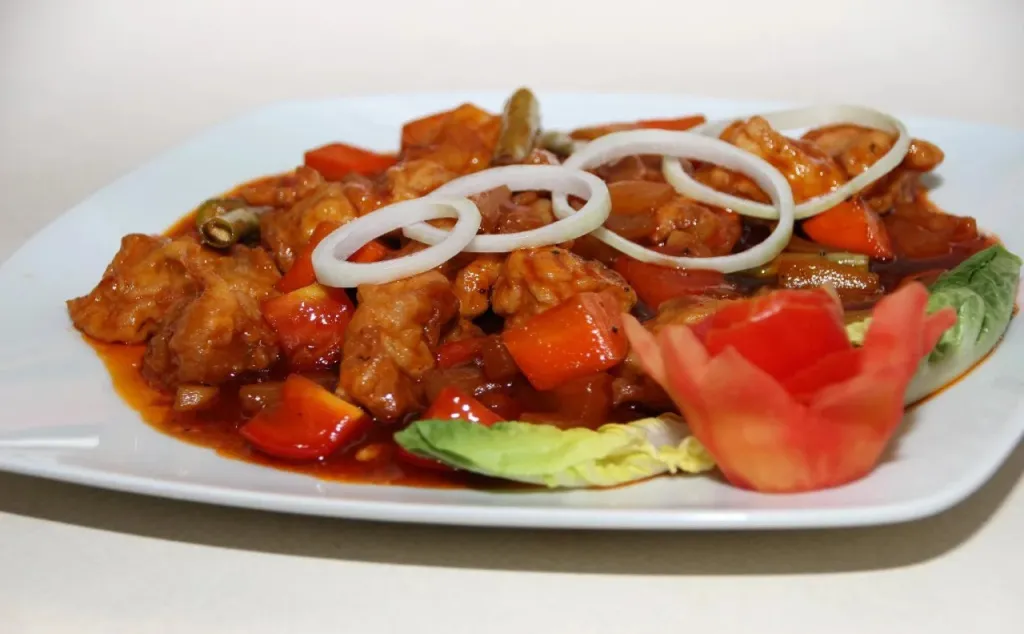 Assiette de poulet aigre-doux décorée de légumes et d'oignons.