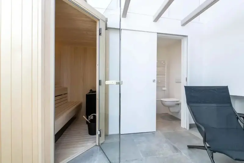 Une salle de bain moderne s'ouvre sur un sauna en bois clair.