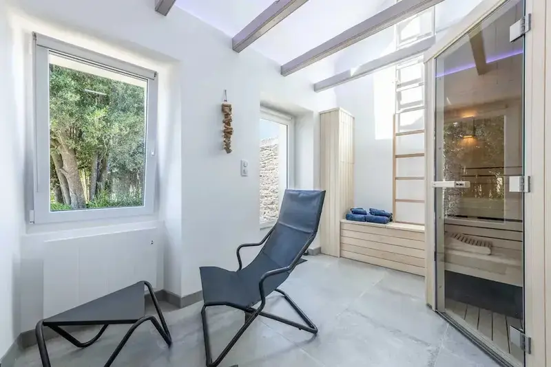 Espace de détente intérieur avec chaise longue et sauna en verre.