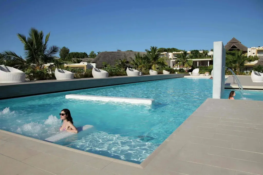 Une piscine rectangulaire avec des personnes se baignant et des chaises longues blanches.