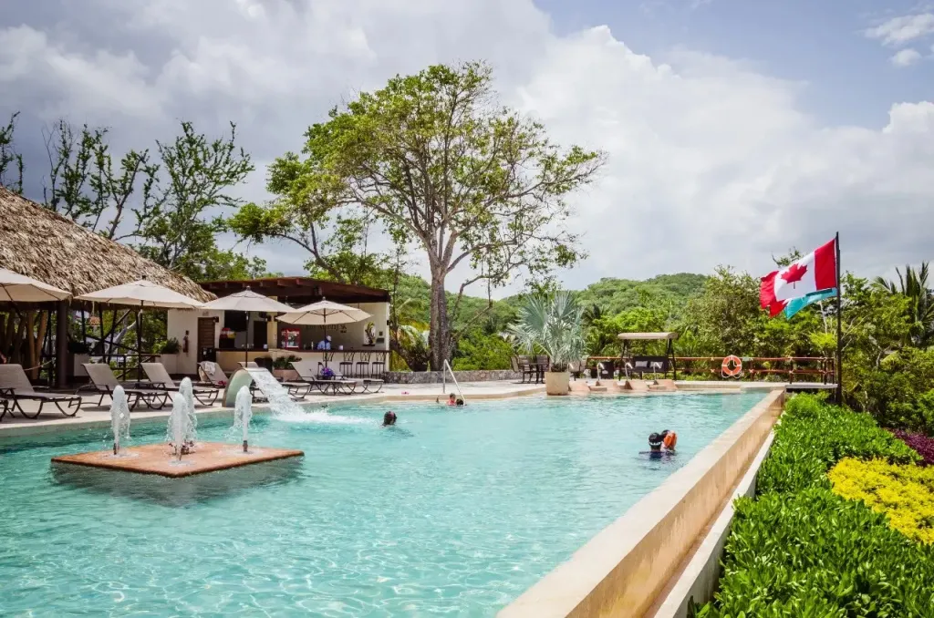 Une piscine rectangulaire avec des fontaines et des transats sous des parasols.