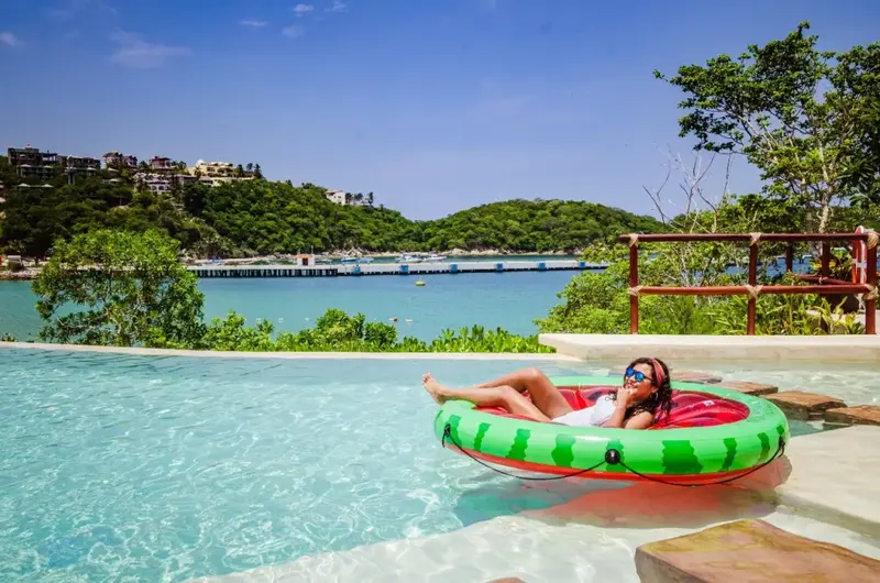 Une femme se détend sur un flotteur dans une piscine à débordement avec vue sur la mer.