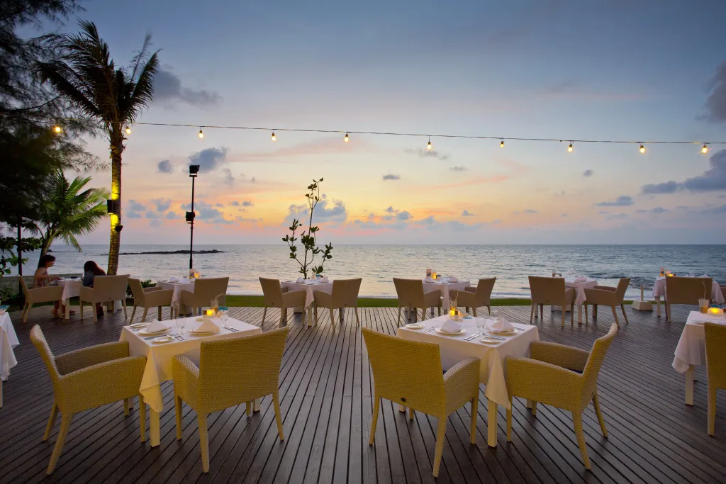 Tables dressées en terrasse face à la mer au coucher du soleil.