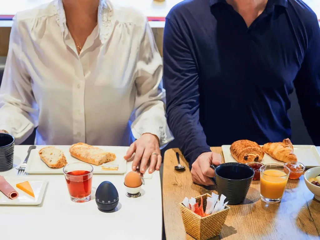 Une table est dressée avec des viennoiseries, des boissons et de la confiture.