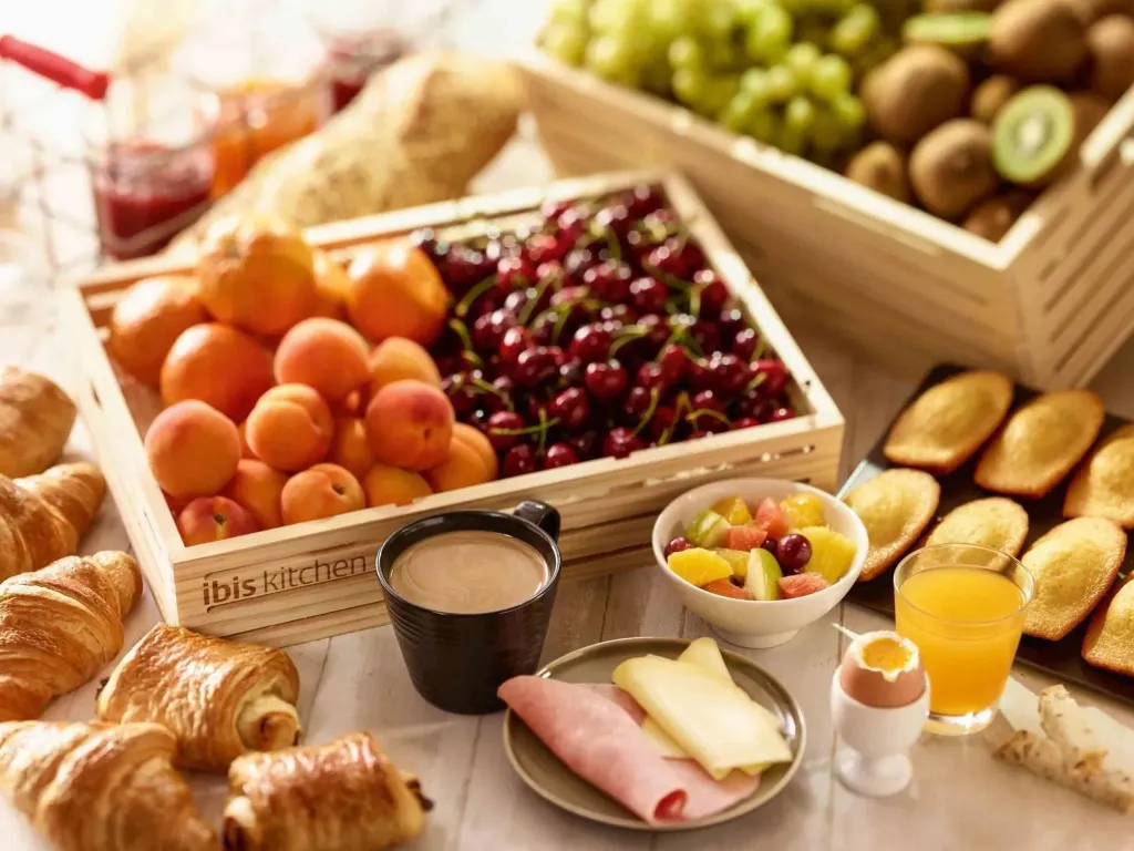 Une table garnie de viennoiseries, de fruits frais, de charcuterie et de boissons.
