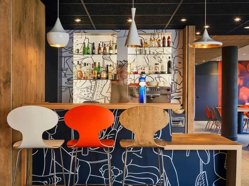 Un comptoir de bar moderne avec des tabourets colorés et une décoration murale graphique.