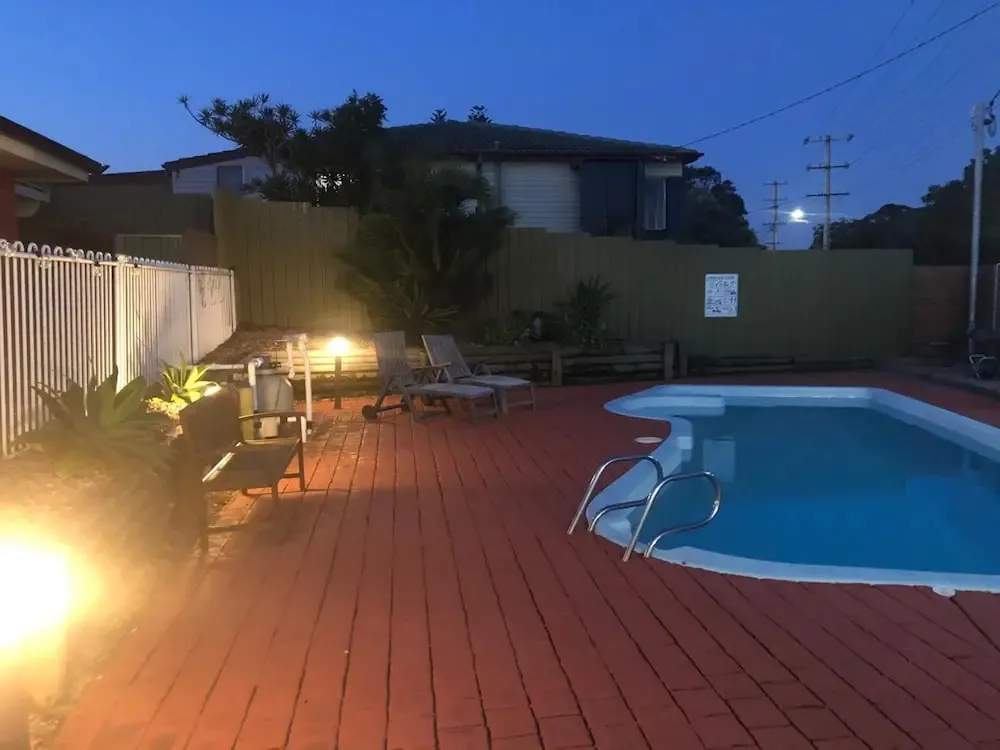 Une piscine rectangulaire est entourée d'une terrasse pavée et de quelques transats.